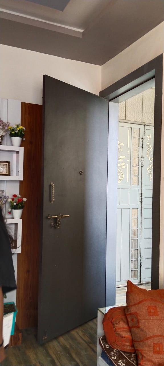 Interior view of a dark-colored flush door within a living space, featuring white walls and wooden flooring. (Source: CKA Archives)