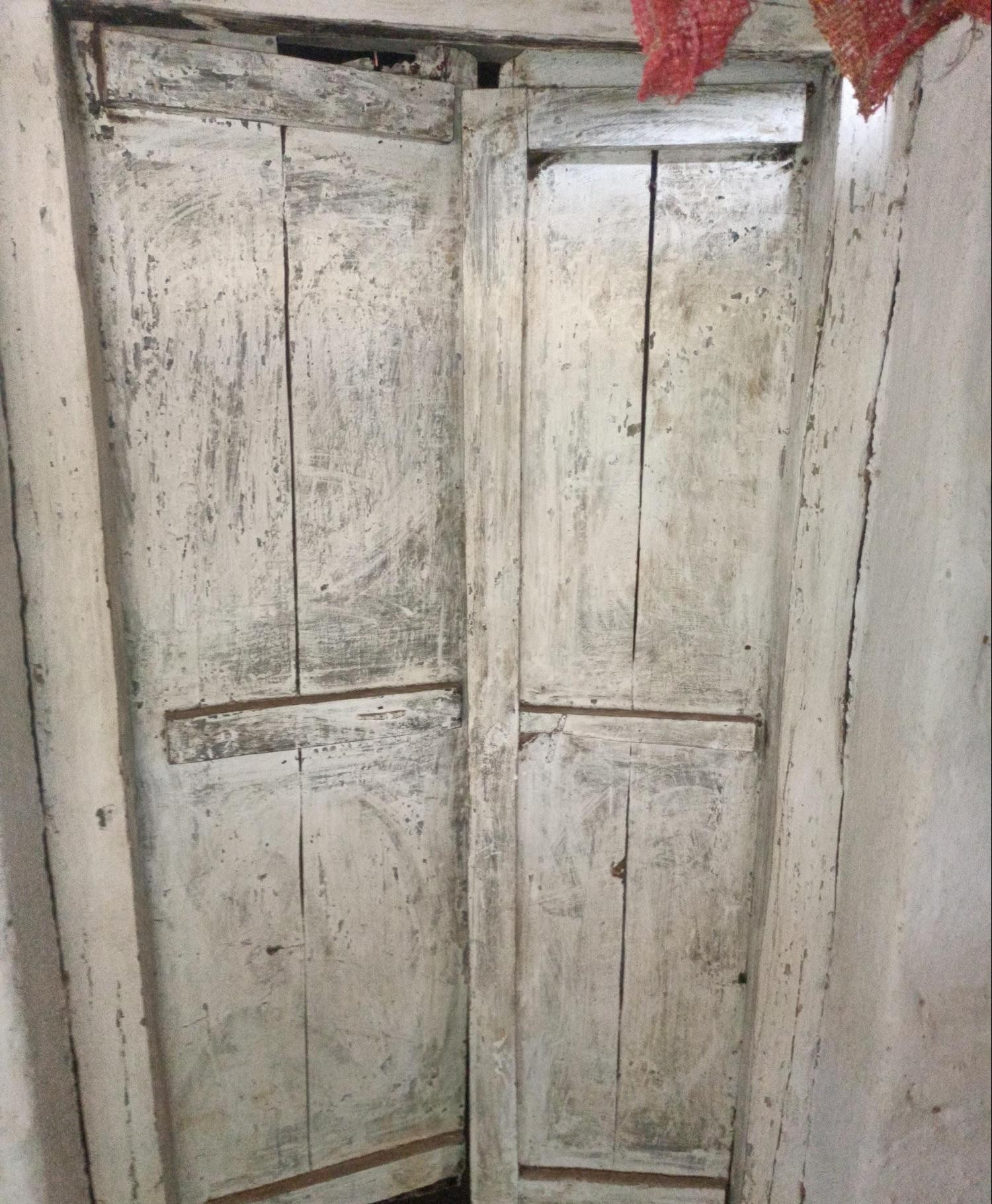 Weathered wooden door painted in white, showing a simple paneled design and signs of aging. (Source: CKA Archives)