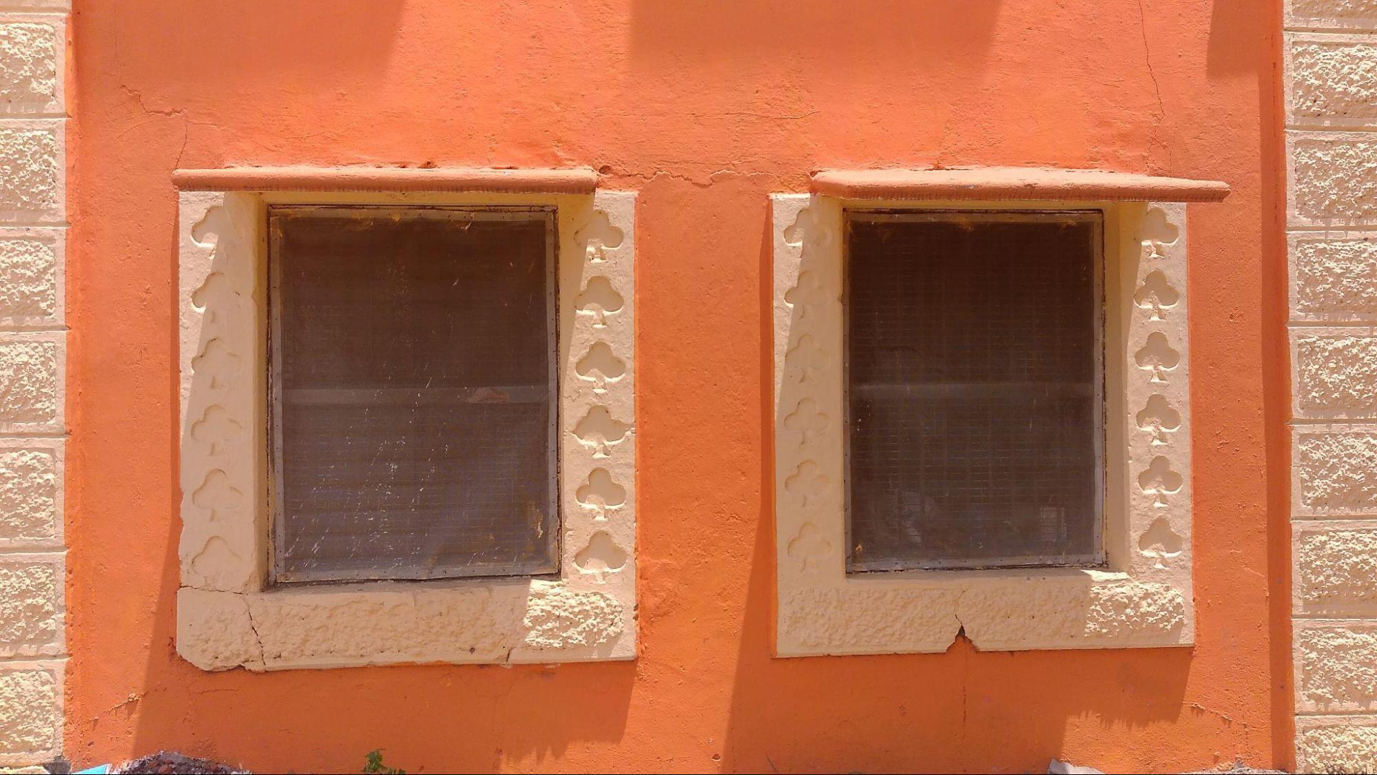 Close-up of a window with decorative grill work and protective netting. Notice the designs which can be seen on the rectangular shaped niches of the property. The design may resemble trees or a four-leaf clover. (Source: CKA Archives)