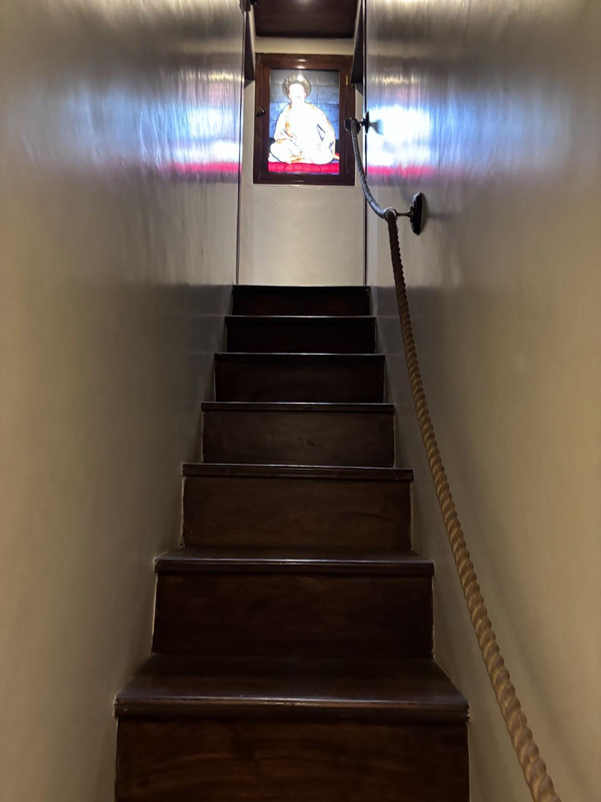 A narrow wooden staircase inside the wada, with a photograph of Bhausaheb Laxman Javale displayed at the landing. (Source: CKA Archives)