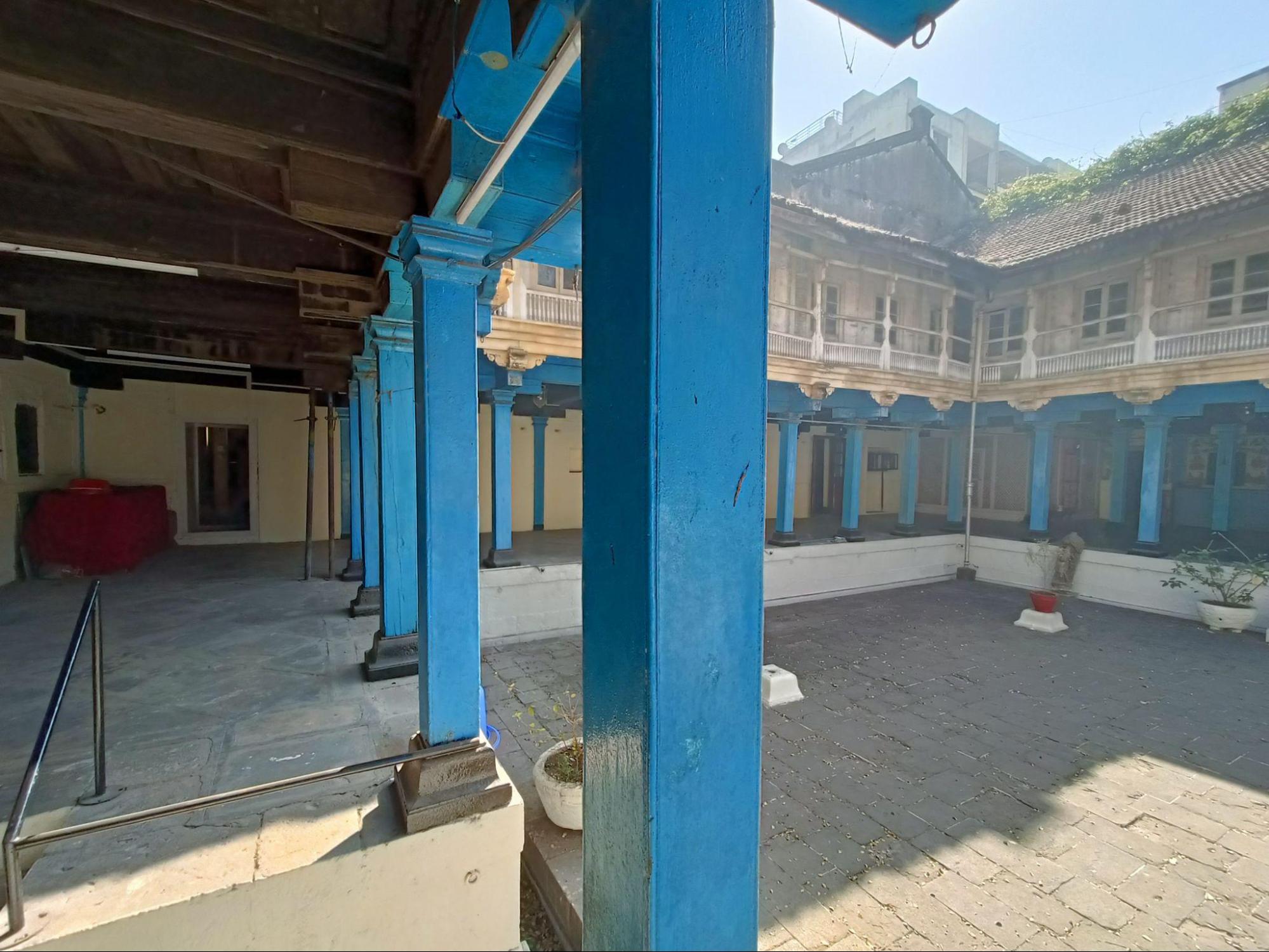 The vibrant blue on the wooden pillars give the structure an aesthetic look. Notably, the pillar’s construction, with a stone base, is a typical feature of wada architecture. Additionally, notice the unique roofing system, featuring a ‘gable end’ at the far right corner, beneath which the roof slopes. (Source: CKA Archives)