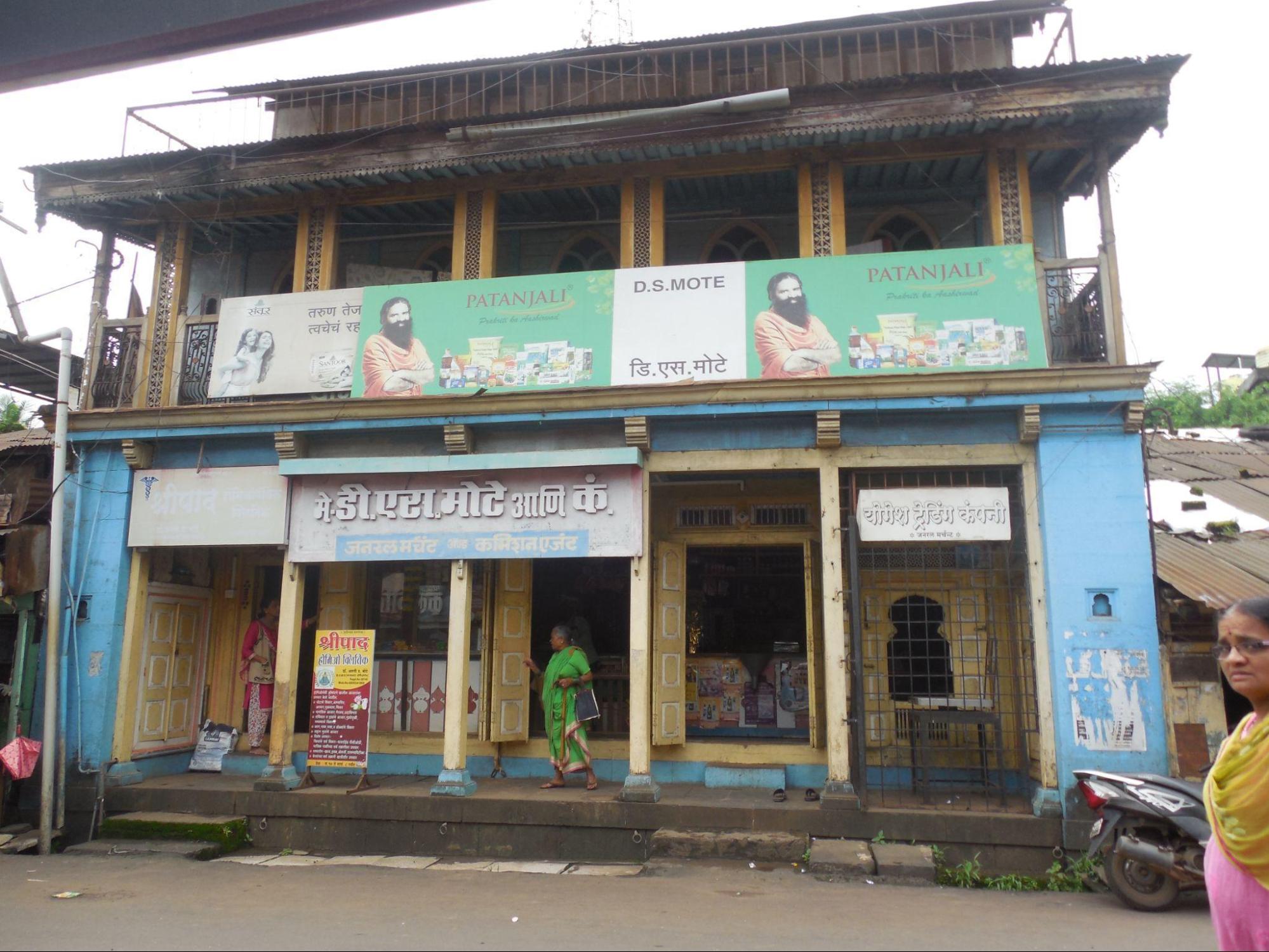 Front view of the residential building. One notices a shop on the ground floor, which seems to be frequented by locals. An advertisement hoarding of Patanjali is hung up on the first floor balcony. (Source: CKA Archives)