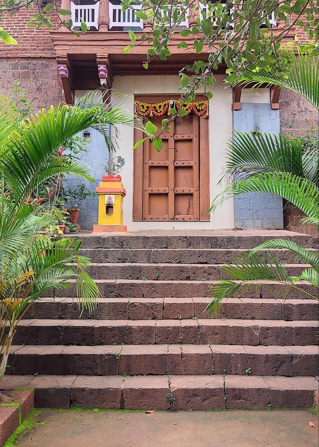 View of the entrance steps at Bakulicha Wada. The elevated plinth and wide stone staircase give the building a commanding presence from the street. A Tulsi Vrundavan sits at the threshold, while a marigold toran marks the main wooden doorway.(Source: CKA Archives)