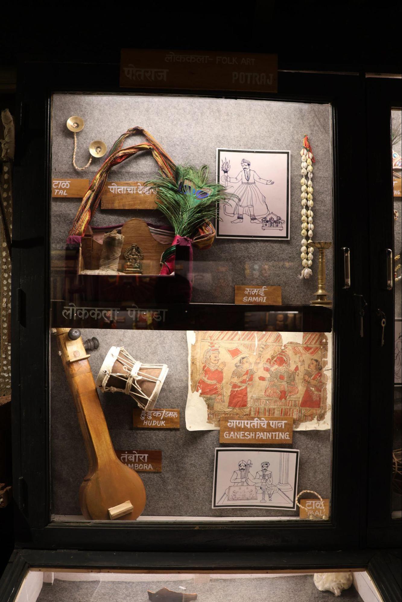 Instruments used in Powada performances from Sindhudurg—huduk (drum), tambora (string instrument), and taal(cymbals)—are displayed here alongside a traditional Ganesh painting and an illustration of performers. (Source: CKA Archives)