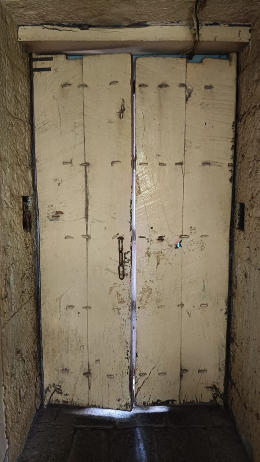 Internal wooden door of the residence, painted a solid neutral color and secured with a chain and padlock. (Source: CKA Archives)